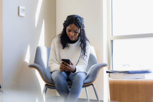 Stressed young adult woman looks at social media on phone Sitting alone, the stressed and worried young adult woman looks at social media posts on her smart phone. serious black teen stock pictures, royalty-free photos & images