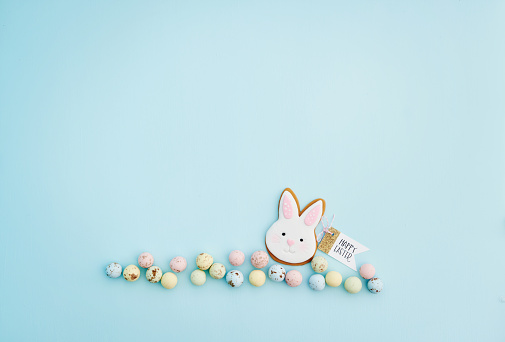 Pastel Easter background with Easter bunny cookie decoration and HAPPY EASTER message amongst pastel chocolate speckled Easter egg candy