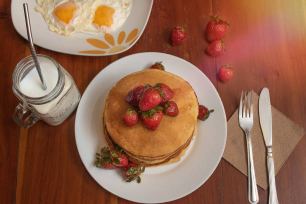 Plate of hot cakes with strawberries and eggs on a table stock photo