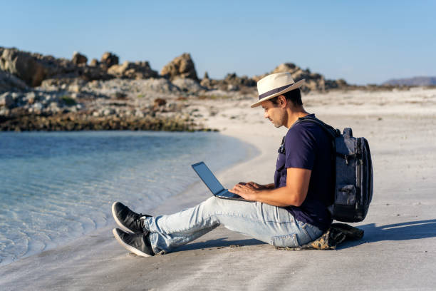 istock latin man sitting on the beach with laptop alone doing telecommuting or remote work 1386092509