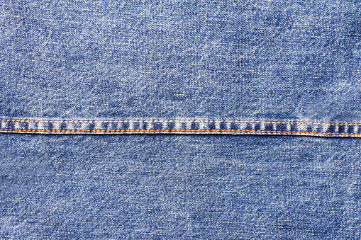 Texture backdrop photo of blue colored denim cloth with seam.