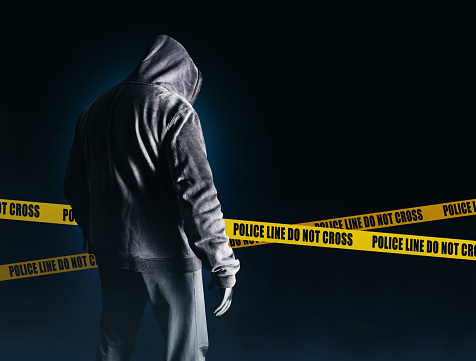 Photo of scary horror stranger stalker man in black hood and clothing on dark blue background with police lines.