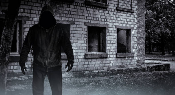 istock Stalker man in black hood on abandoned building backdrop. 1386097129