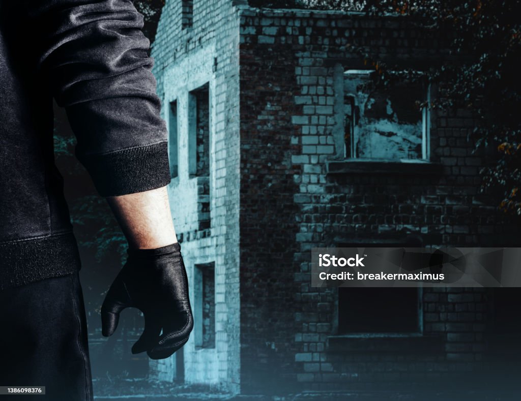 Stalker person in black outfit and gloves. Photo of dangerous criminal stalker man in black outfit and gloves standing on abandoned building background. Kidnapping Stock Photo