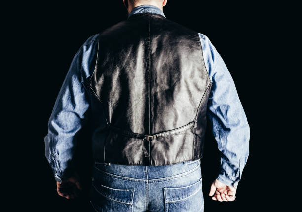 Man in jeans shirt and leather vest on black background. stock photo