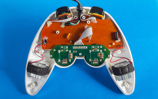Photo of classic disassembled wired modern silver colored game pad controller laying on blue background.