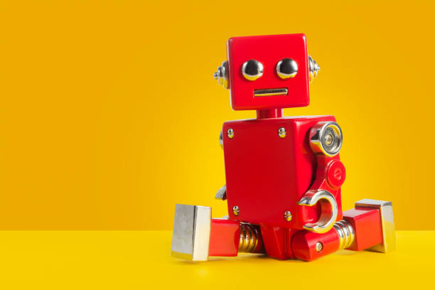 Red colored robot toy leg-split sitting on orange background. stock photo