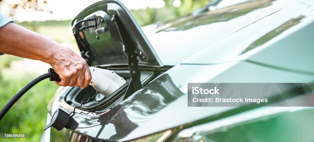 Human hand is holding electric car charging connect to electric car Car Stock Photo