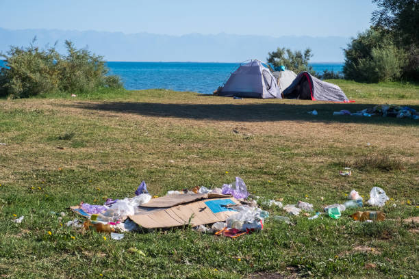 istock Environment  pollution by tourists problem concept. Waste, trash on the wild beach with tourists tents on background. Ecology concept. 1386111020