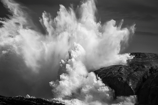 Black and white powerful ocean waves crashing against rocky coastline