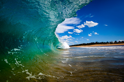 Inside barrel of green ocean wave looking at beach