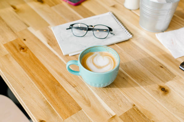 istock Cappuccino coffee in blue cup and eyeglasses, notebook on light table in cafe. 1386154923