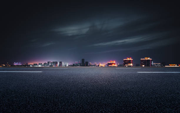 la vista nocturna de la ciudad frente a la carretera de asfalto - ciudad fotografías e imágenes de stock