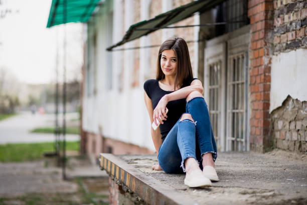 Teenage girl with brown hair, seen from behind, climbing a vibrant red metal wall while dressed in a trendy striped shirt and stylish flared jeans, embodying youthful exploration and freedom