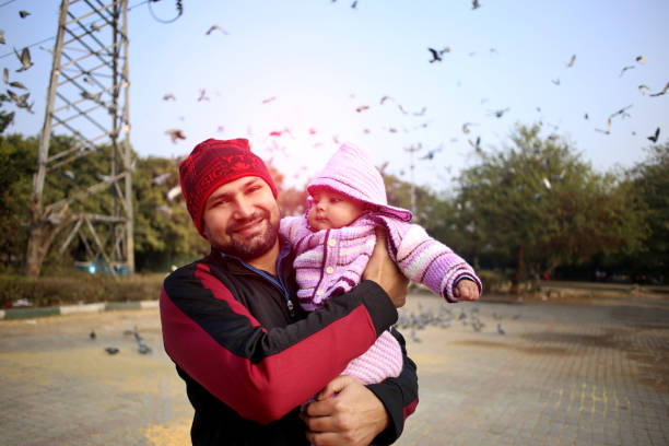 Young men holding his lovely daughter outdoors in public park during sunset time.