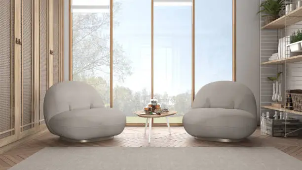Minimalist living room in japanese style in white tones, armchair, carpet and parquet floor. Tea time, glass teapot and teacup, snacks. Big panoramic window, modern interior design