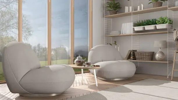 Minimalist living room in japanese style in white tones, armchair, carpet and parquet floor. Tea time, glass teapot and teacup, snacks. Big panoramic window, modern interior design