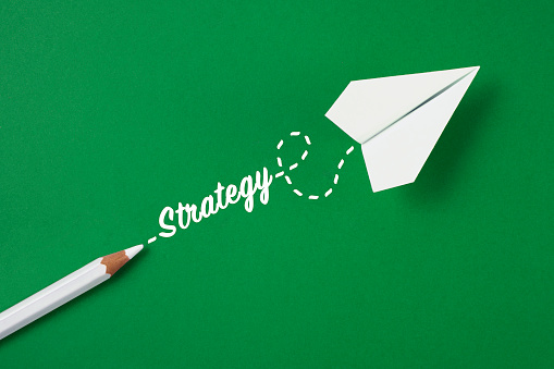White colored crayon with Strategy text and an white colored paper plane on green background