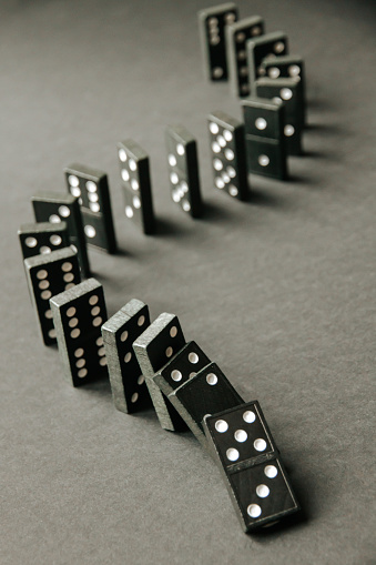 Black dominoes chain on a dark table background. Domino effect concept