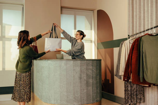 cheerful clothing store owner assisting a female customer - fashion store imagens e fotografias de stock