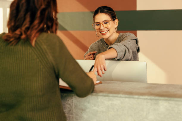 réceptionniste décontractée aidant une femme à se connecter à un bureau - hotel receptionist photos et images de collection