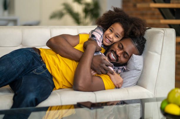 istock Girl looking at camera hugging dad lying on sofa 1386176548