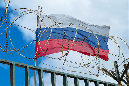 Bandera rusa detrás de alambre de púas contra cielo nublado photo