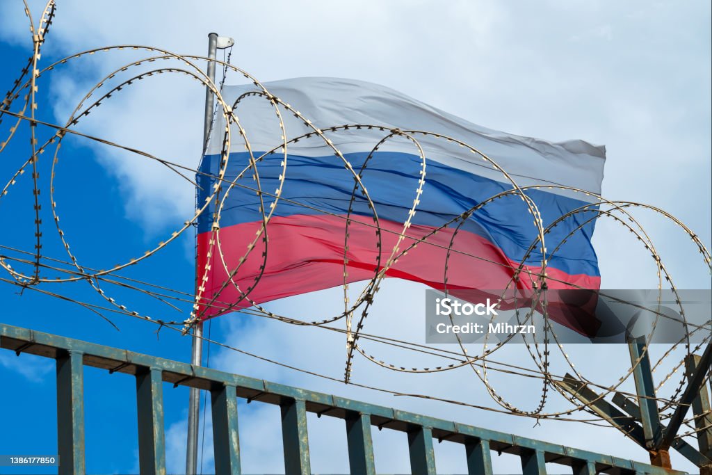 Russian flag behind barbed wire against cloudy sky View of russian flag behind barbed wire against cloudy sky. Concept. Russia Stock Photo