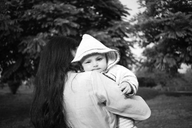 Mother holding her baby daughter in hand outdoors in public park.