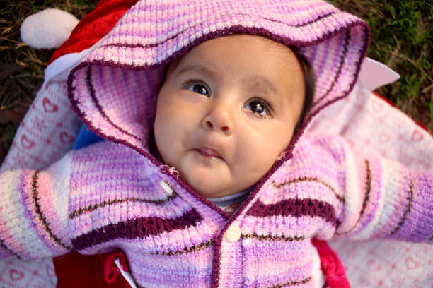 Cute baby girl laying in grass and playing in public park outdoors, Delhi, India.