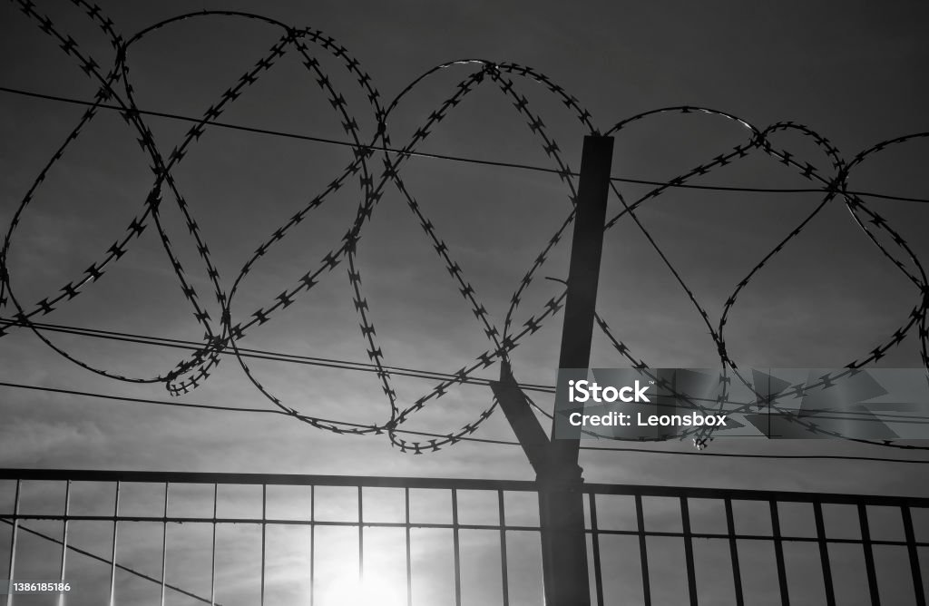 Barbed wire fence at the border The Fence - Low sun behind razor wire (NATO-Draht). Symbol of hope for a better future. International Border Barrier Stock Photo