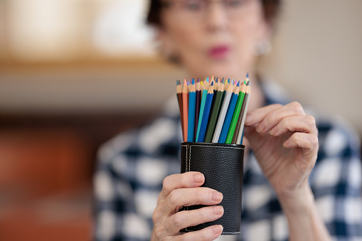 Woman holding a group of colored pencils and selecting one. Focus is on the pencils.