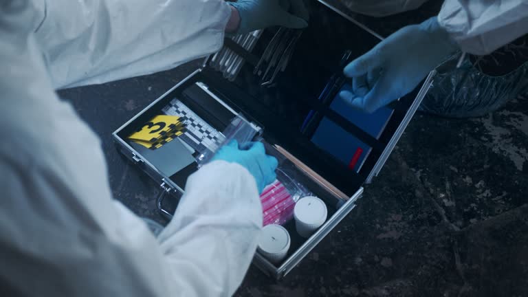 Close up of a criminologist in a protective suit opening a  kit and giving a something to a colleague