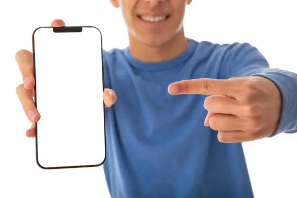 Excited mixed race teenager wearing blue showing mobile phone on cut out white background