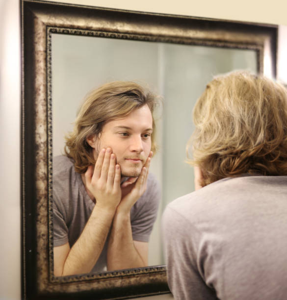 istock young man looking in the mirror,combing his hair,looking at problems on face. 1386189873