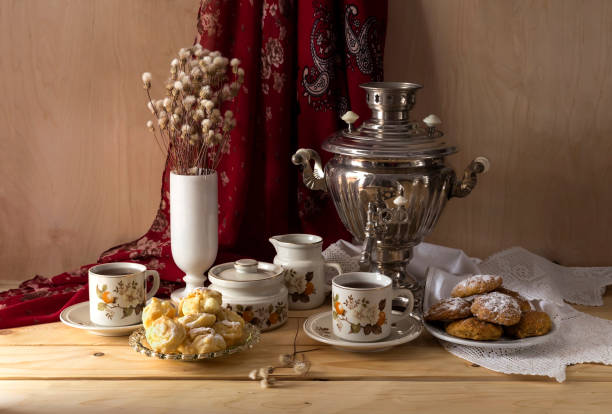 Still-life in Russian style with an old samovar, tea in cups, biscuits and cakes on a wooden table close-up