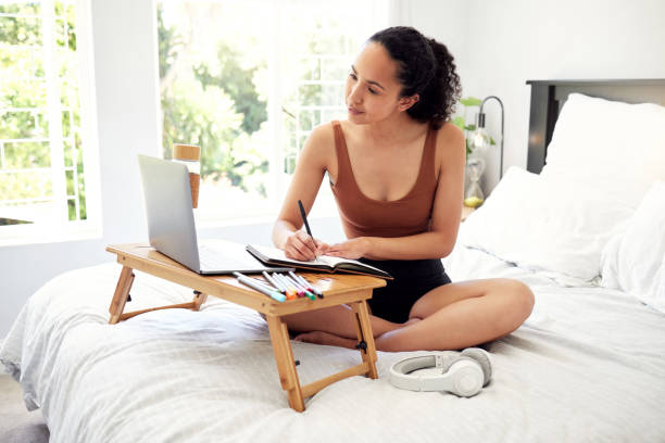 istock Shot of a young woman using a laptop while writing in a notebook at home 1386195850