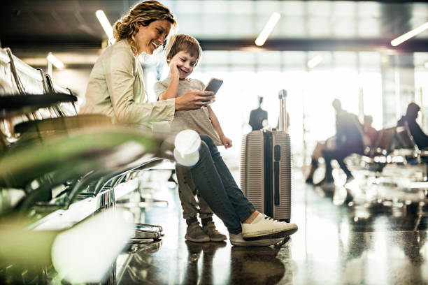 Single mother and son using cell phone while waiting for their transportation at departure area.