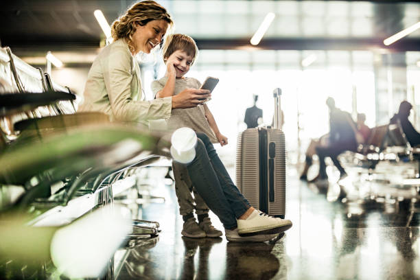 Single mother and son using cell phone while waiting for their transportation at departure area. Happy mother and her small son using smart phone while waiting for their flight at departure area. travel destinations family stock pictures, royalty-free photos & images