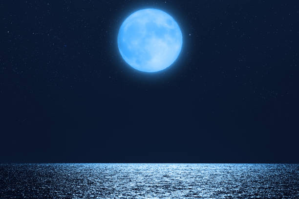 istock Full Moon with starry skies rising above ocean horizon. 1386197945