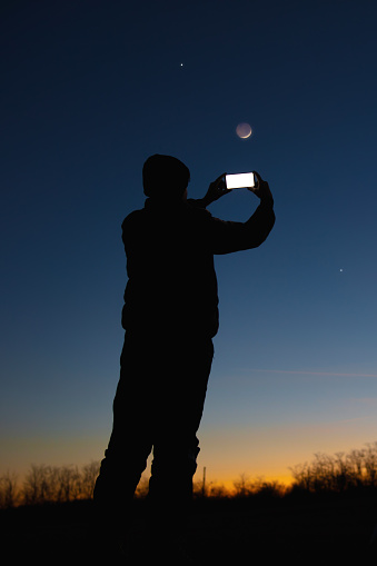 Silhouette of a man with smartphone and countryside under evening skies.