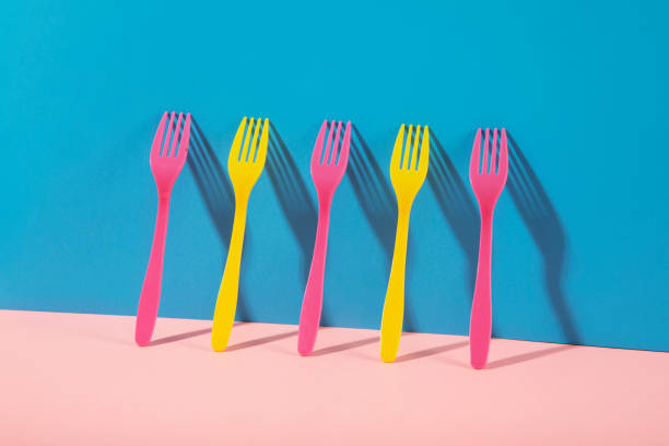 Close up of plastic yellow and pink colored forks in a row on two toned beige and pink background