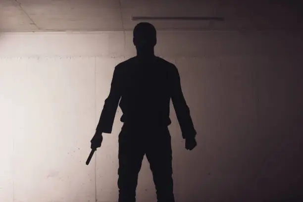 silhouette of an armed man holding his gun and pointing with his laser beam at a target.