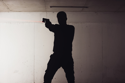 silhouette of an armed man holding his gun and pointing with his laser beam at a target.