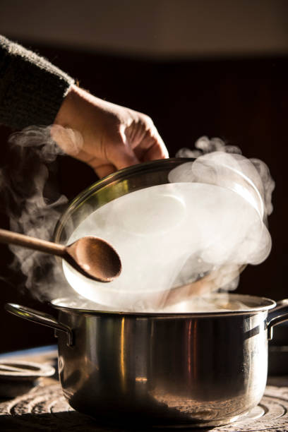 Wooden spoon over a hot metal pot while cooking a meal on a gas stove. Selective focus.