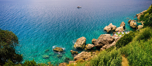 Beautiful panoramic landscape of nature of the Mediterranean coast with top view of huge stones and rocks in water, turquoise sea surface with waves and small white boat.