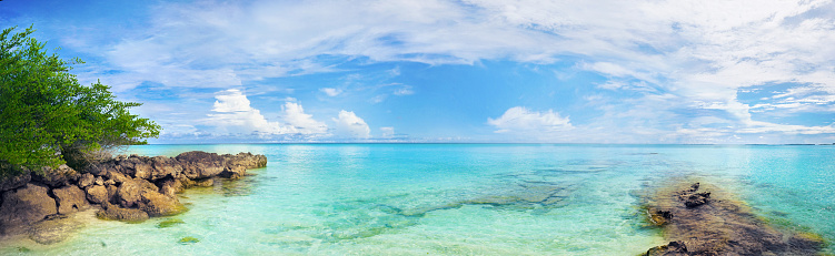 Beautiful tropical panoramic landscape with clear turquoise ocean water, rocks and blue sky with white clouds.