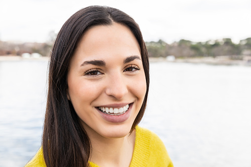 Close-up of affective girl with long hair smiling at camera having fun in nature. Beautiful Latin woman with the lake in the background.