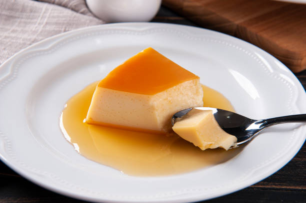 istock Delicious condensed milk pudding on white plate. Someone scooping up a piece with a spoon. 1386212655