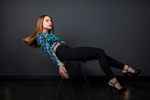 Young model sitting on chair posing as if her feet are flying in the air. Her hair is still in the air, her hands and feet are in the air.